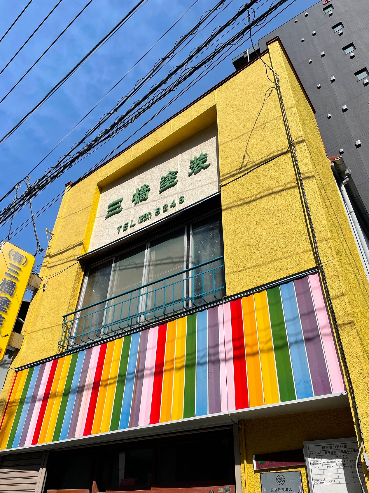 宮川町の社屋。黄色い外壁に緑の立体文字「三橋塗装」の看板と虹のストライプ幕板